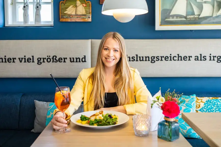 Kaamp Meren Kampen: Finja am Tisch im Innenraum mit Getränk in der Hand und Essen vor sich