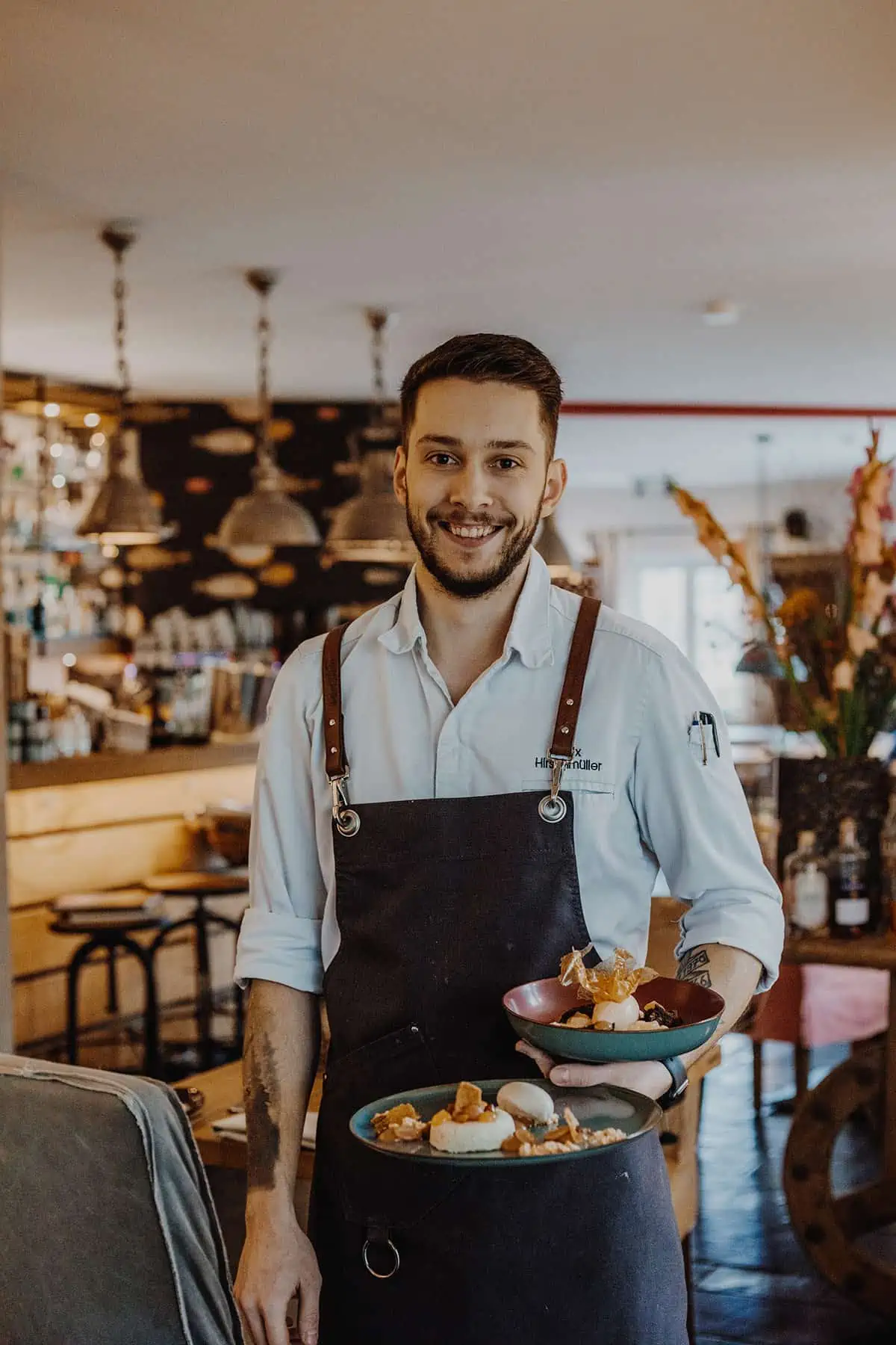 Restaurant & Weinbar Coast: Portrait von Felix Hirschmüller mit Tellern in der Hand