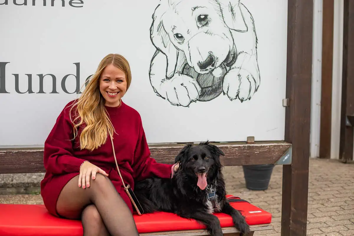 Sylt Fräulein Finja sitzt mit einem schwarzen Hund vor Dogstyler Sylt